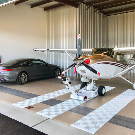 Plane and Mercedes parked in a hangar with RaceDeck CircleTrac flooring and white Free-Flow accents.